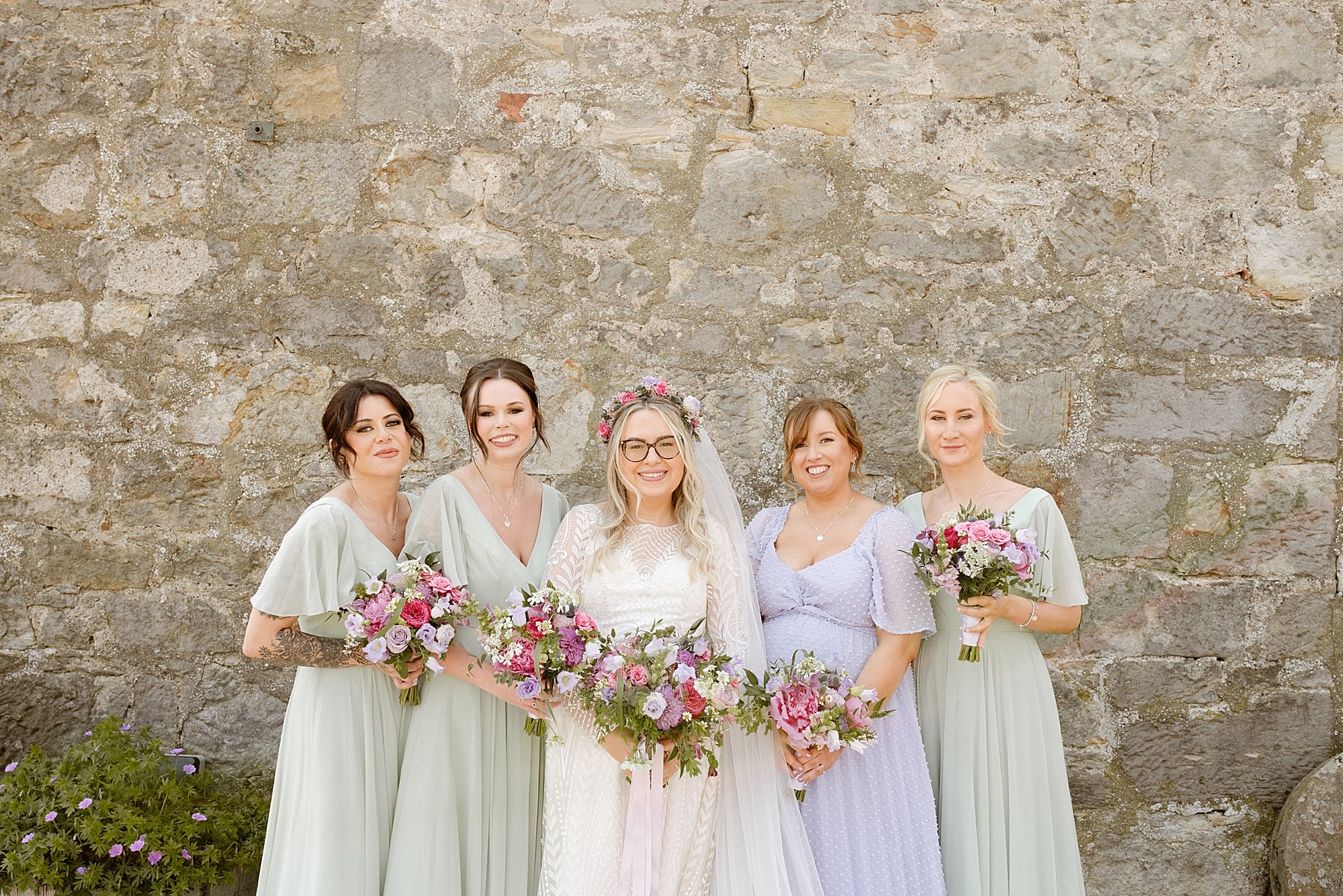bride and her bridesmaids dressed in mint green and lavender bridesmaid dresses in front of a stone wall at the den at culross