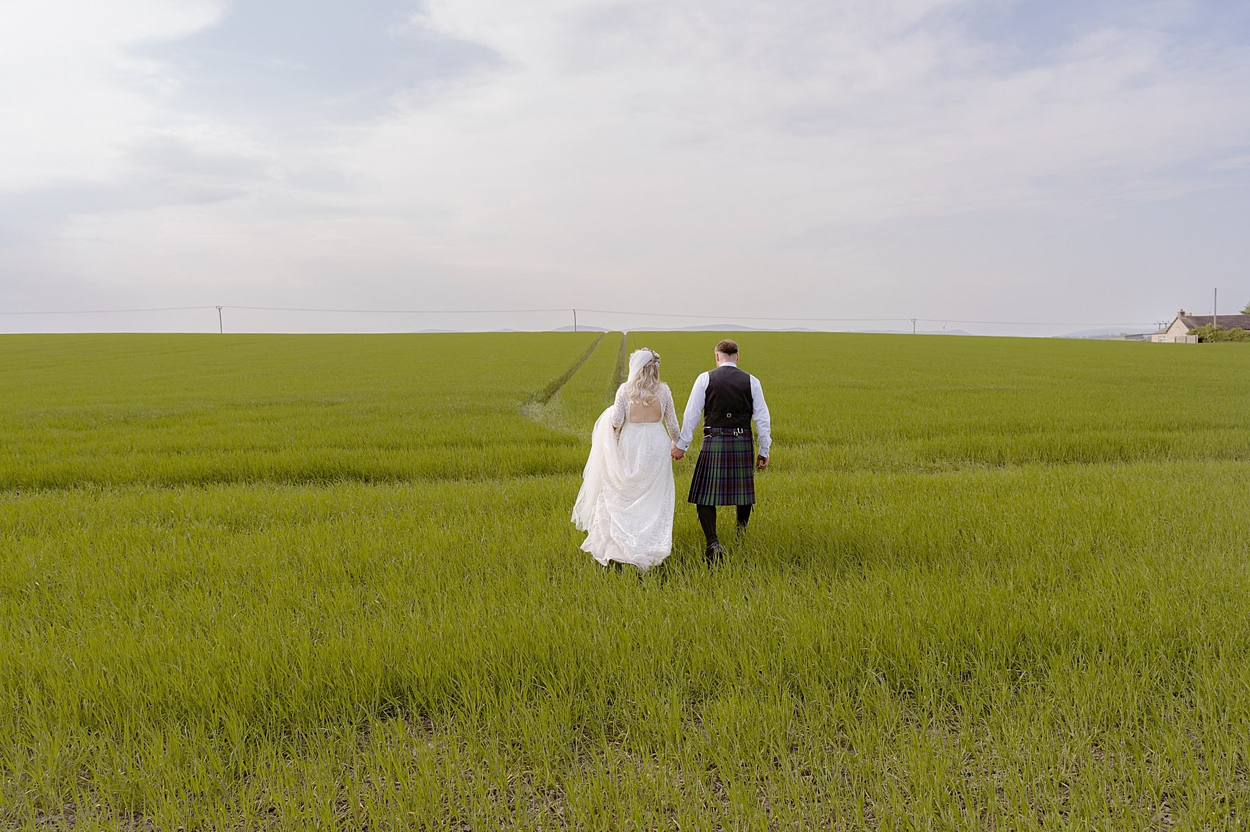 bride and groom walking in green field after their the den at culross wedding ceremony