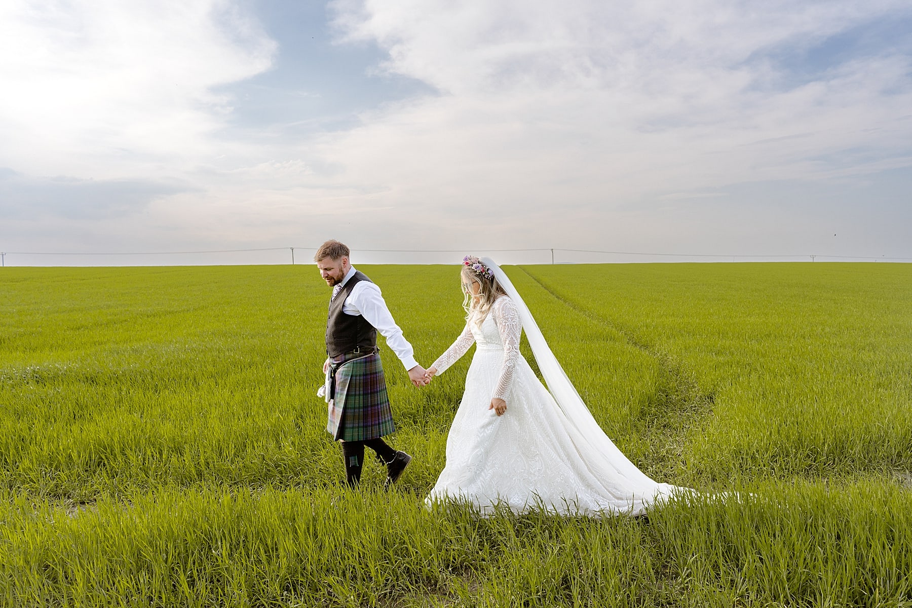 bride and groom walking in green field after their the den at culross wedding ceremony scotland