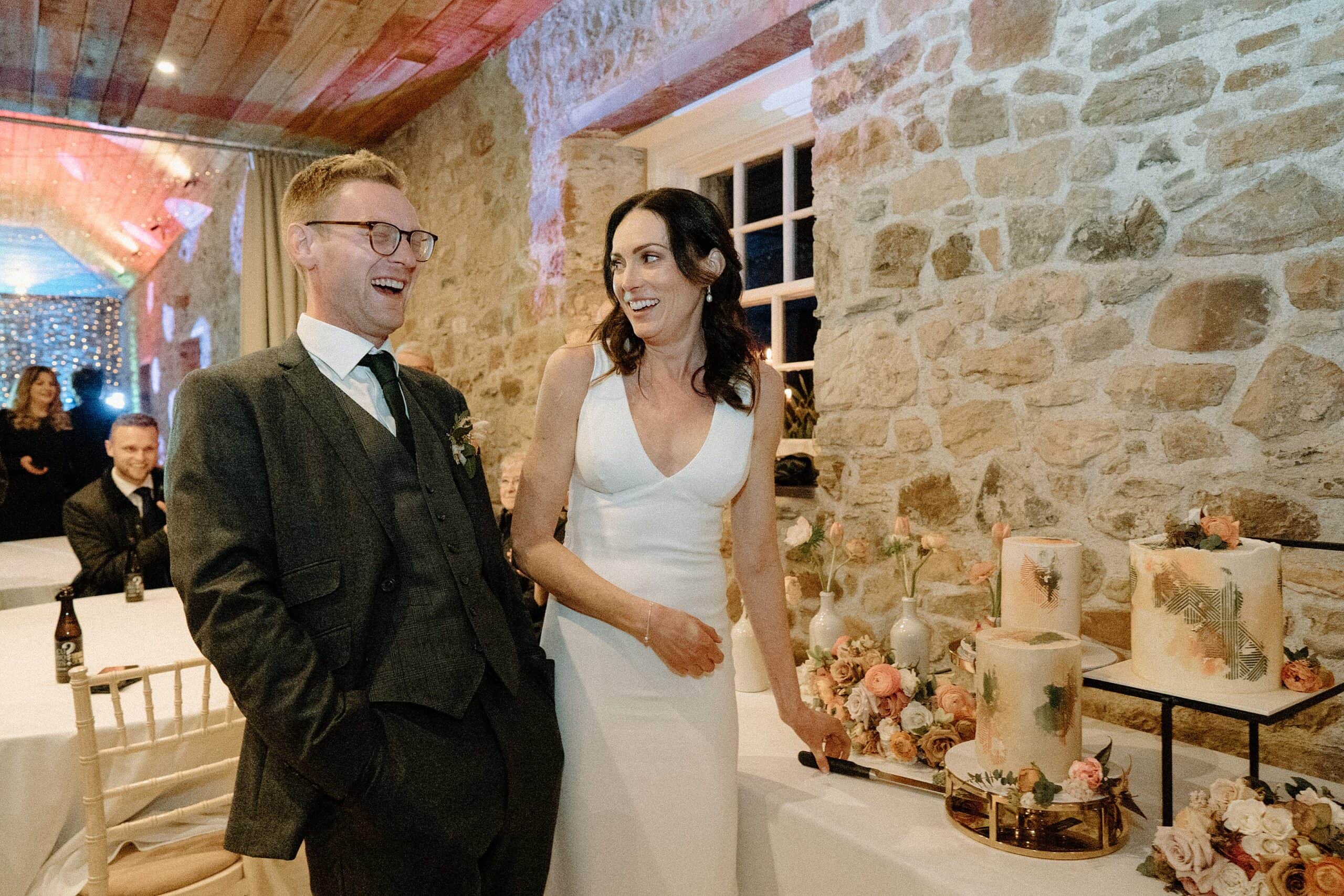 the bride and groom cut their wedding cake following their joyful wedding ceremony at a farm wedding venue in east lothian in scotland