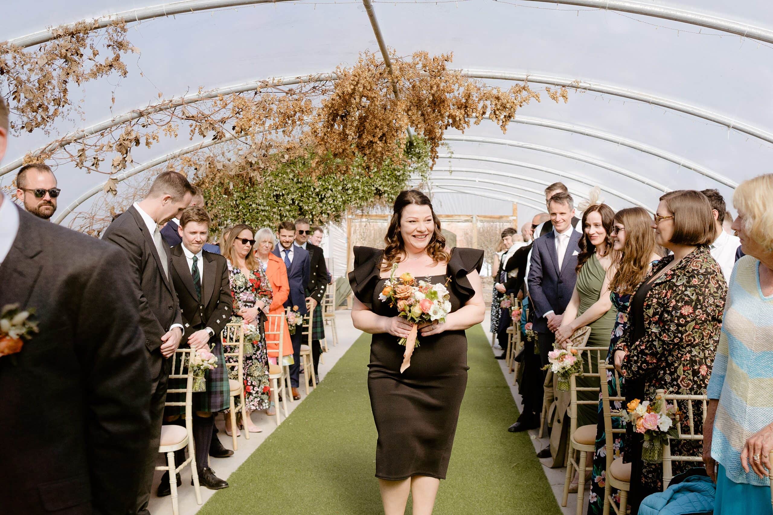 a smiling bridesmaid walks down the aisle as standing guests watch in unusual wedding venues east lothian scotland