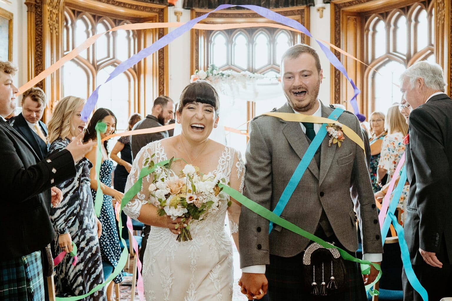 bride and groom being covered in colourful ribbons as they walk back down the aisle wedding trends scottish wedding photographer