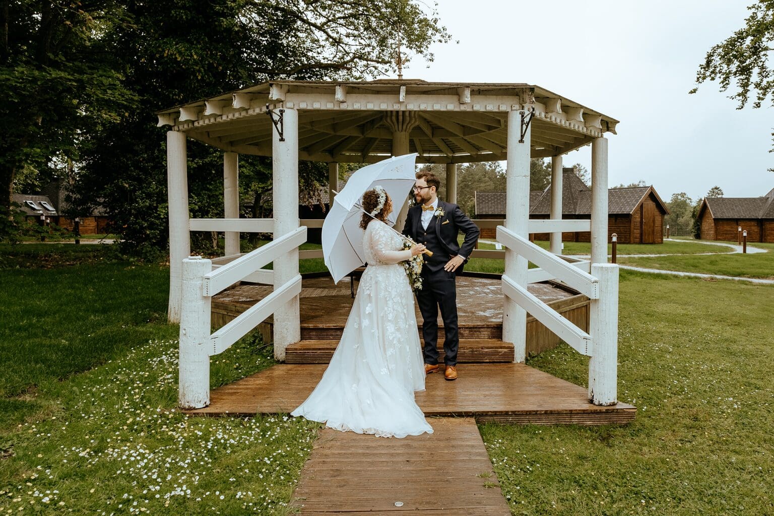bride and groom standing on front of wooden gazebo in the rain bride holding white umbrella what to do if it rains on your wedding day scottish wedding photography